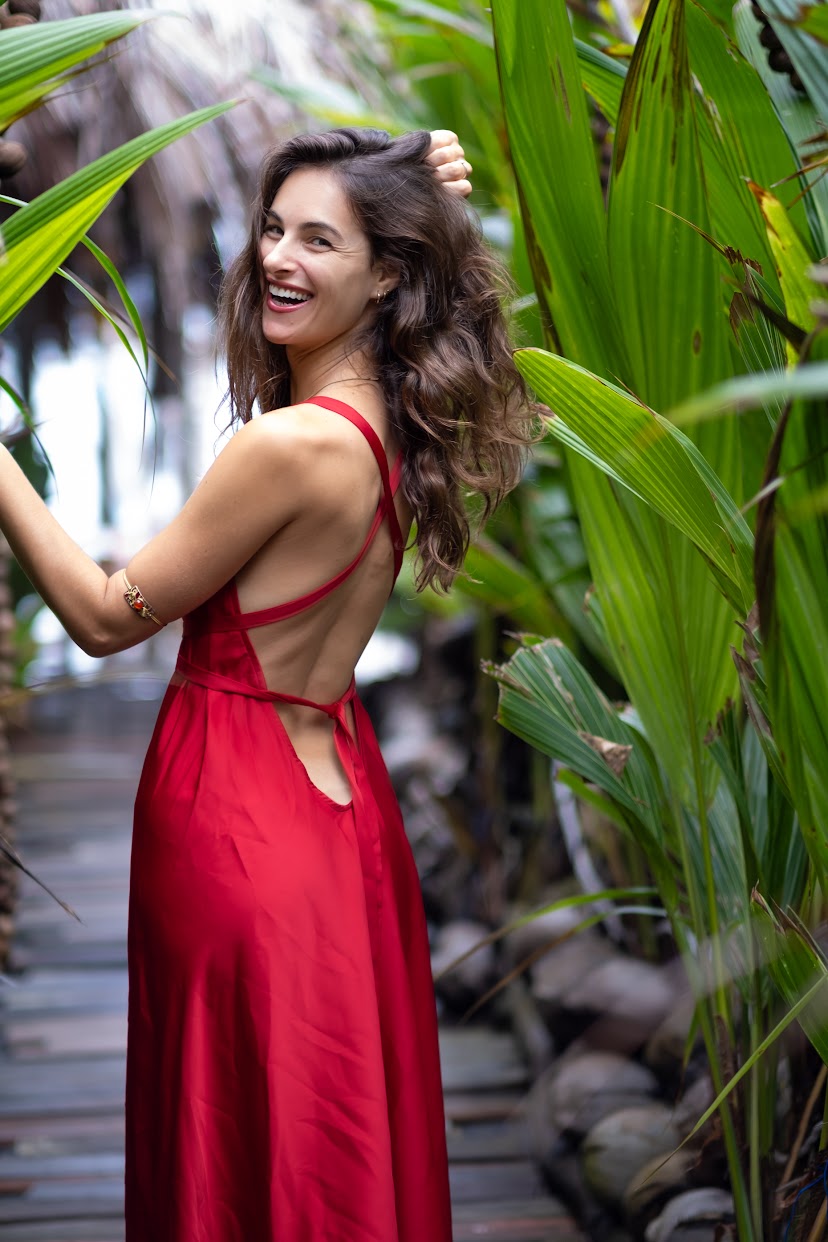 Danielle smiling in a red dress among tropical palms